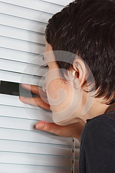 Young woman looking through the blinds of light room