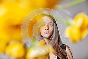 Young woman looking at camera behind yellow flower