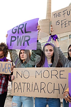 Young woman looking at camera holding No more patriarchy banner in feminist demonstration for woman& x27;s rights. Vertical. photo