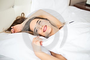 Young woman looking at camera and smiling while lying on the bed at home