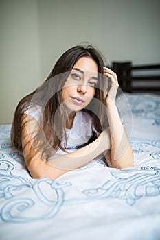 Young woman looking at camera and smiling while lying on the bed at home