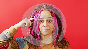 Young woman looking at camera and twirling finger at her temple on red background. Portrait of perplexed female in state