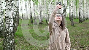 A young woman is looking for a cellular network in a birch forest. A girl is talking on the phone, but the connection is