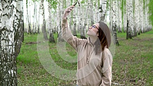 A young woman is looking for a cellular network in a birch forest. A girl is talking on the phone, but the connection is