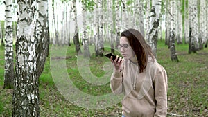 A young woman is looking for a cellular network in a birch forest. A girl is talking on the phone, but the connection is