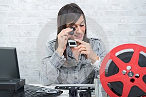Young woman looking at film slide with magnifying glass