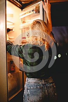 Young woman looking for food in refrigerator at night at home