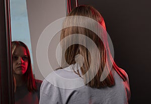 Young woman looking at her mirror reflection with grief. Unhappy sad person. Psychological concept of mental disorders