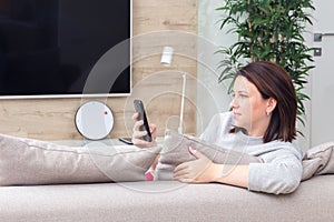 Young woman looking at her smart phone and smiling while sitting on the couch