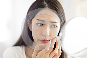 Young woman looking at  mirror and checking the  acne problem at home