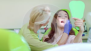Young woman looking at mirror in dentist chair. Female dentist curing patient