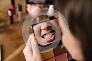 Young woman looking at mirror while doing makeup indoors