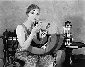 Young woman looking into a mirror and putting on make up