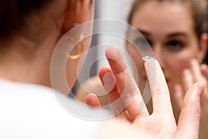 Young woman looking in mirror to change her contact lens