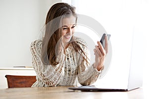 Young woman looking at mobile phone and computer