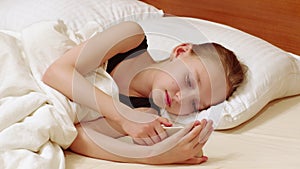 Young woman looking mobile phone lying in white bed. Teenager girl using smartphone in white bedroom lying in cozy bed.