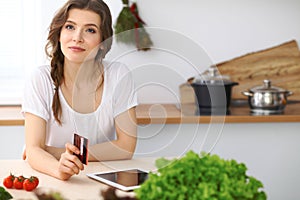 Young woman looking for a new recipe for cooking in a kitchen. Housewife is making online shopping by tablet comput