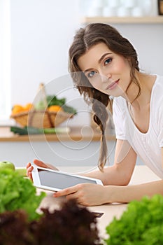 Young woman looking for a new recipe for cooking in a kitchen. Housewife is making online shopping by tablet comput