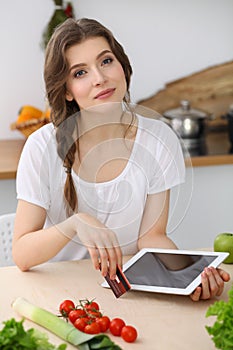 Young woman looking for a new recipe for cooking in a kitchen. Housewife is making online shopping by tablet computer