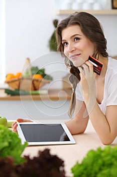 Young woman looking for a new recipe for cooking in a kitchen. Housewife is making online shopping by tablet computer