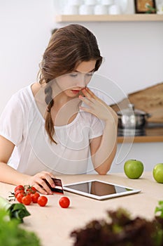 Young woman looking for a new recipe for cooking in a kitchen. Housewife is making online shopping by tablet computer