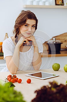 Young woman looking for a new recipe for cooking in a kitchen. Housewife is making online shopping by tablet computer