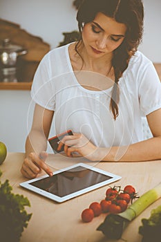 Young woman looking for a new recipe for cooking in a kitchen. Housewife is making online shopping by tablet computer