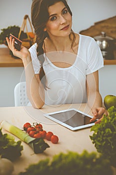 Young woman looking for a new recipe for cooking in a kitchen. Housewife is making online shopping by tablet computer