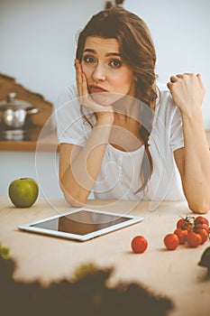 Young woman looking for a new recipe for cooking in a kitchen. Housewife is making online shopping by tablet computer