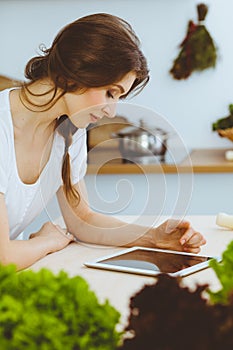 Young woman looking for a new recipe for cooking in a kitchen. Housewife is making online shopping by tablet computer