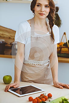 Young woman looking for a new recipe for cooking in a kitchen. Housewife is making online shopping by tablet computer