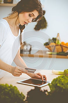 Young woman looking for a new recipe for cooking in a kitchen. Housewife is making online shopping by tablet computer