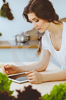 Young woman looking for a new recipe for cooking in a kitchen. Housewife is making online shopping by tablet computer