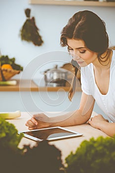 Young woman looking for a new recipe for cooking in a kitchen. Housewife is making online shopping by tablet computer