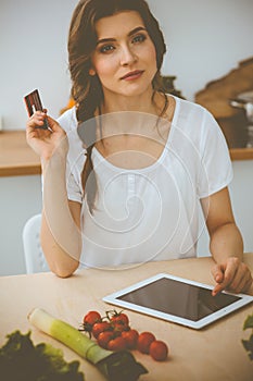 Young woman looking for a new recipe for cooking in a kitchen. Housewife is making online shopping by tablet computer