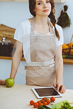 Young woman looking for a new recipe for cooking in a kitchen. Housewife is making online shopping by tablet computer