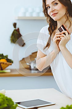 Young woman looking for a new recipe for cooking in a kitchen. Housewife is making online shopping by tablet computer