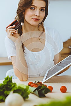 Young woman looking for a new recipe for cooking in a kitchen. Housewife is making online shopping by tablet computer