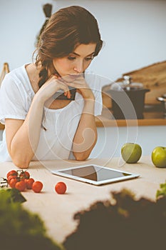 Young woman looking for a new recipe for cooking in a kitchen. Housewife is making online shopping by tablet computer