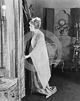 Young woman looking out from behind her curtains