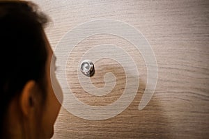 Young woman looking out through the peephole of her front door.