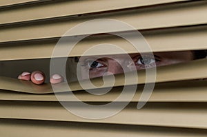 Young woman looking out the window through the blinds