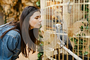 Young woman looking on parrot in cage, pet store