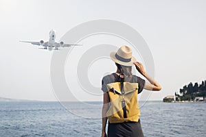 Young woman looking at plane flying above the sea, travel, tourism, enjoy life and active lifestyle concept
