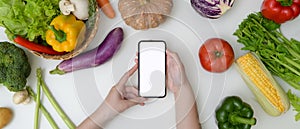 Young woman looking recipe on mock-up smartphone while preparing ingredient for cooking with fresh vegetables