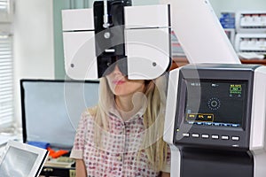 Young woman looking at refractometer eye test machine in ophthalmology