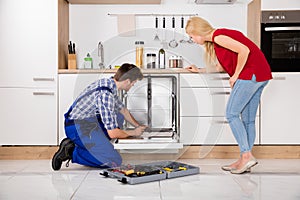 Woman Looking At Repairman Repairing Dishwasher