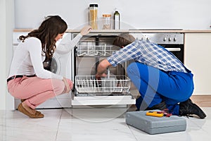 Woman Looking At Repairman Repairing Dishwasher