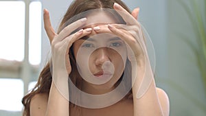 Young woman looking skin face in mirror in bathroom. Woman squeezing acnes