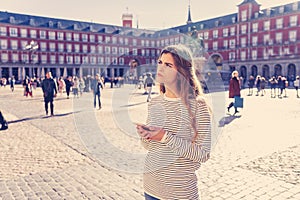 Young woman looking at smart mobile phone in Plaza Mayor Madrid feeling lost looking for directions